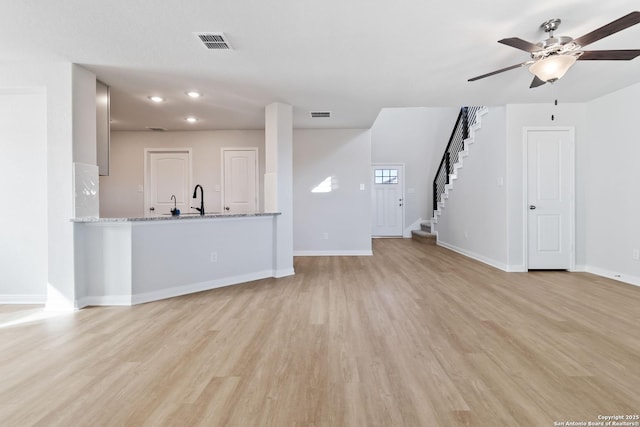 unfurnished living room featuring visible vents, baseboards, ceiling fan, stairway, and light wood-type flooring