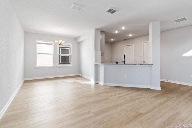 unfurnished living room with light wood finished floors, a chandelier, and visible vents