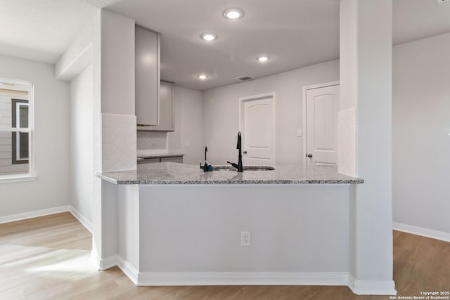 kitchen featuring light stone counters, a sink, light wood finished floors, and gray cabinetry