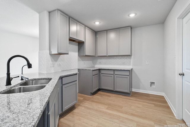 kitchen featuring gray cabinets, light stone counters, a sink, and tasteful backsplash