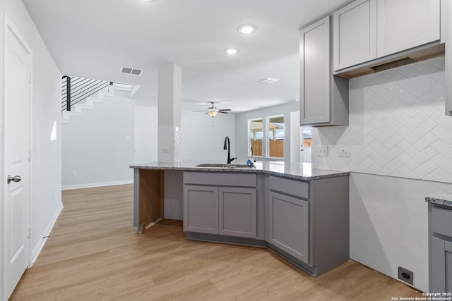 kitchen with decorative backsplash, a ceiling fan, light stone countertops, a sink, and gray cabinetry