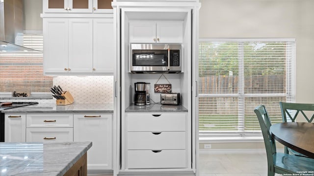 kitchen with decorative backsplash, stainless steel microwave, island exhaust hood, and white cabinetry