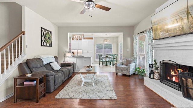 living room with a fireplace, ceiling fan, stairway, and dark wood-type flooring