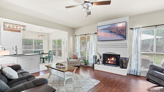 living area with ceiling fan with notable chandelier, dark wood-style floors, and a brick fireplace
