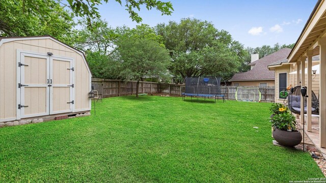 view of yard with a fenced backyard, a trampoline, an outdoor structure, and a shed