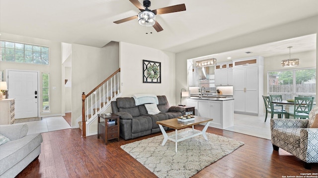living area featuring baseboards, dark wood finished floors, stairway, and ceiling fan with notable chandelier