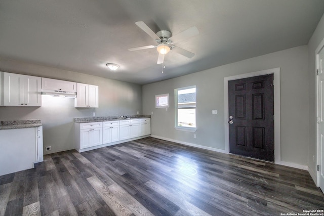 kitchen featuring white cabinets, dark wood-style flooring, a ceiling fan, baseboards, and under cabinet range hood