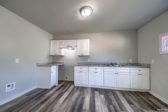 kitchen with white cabinets, a sink, dark wood finished floors, baseboards, and under cabinet range hood