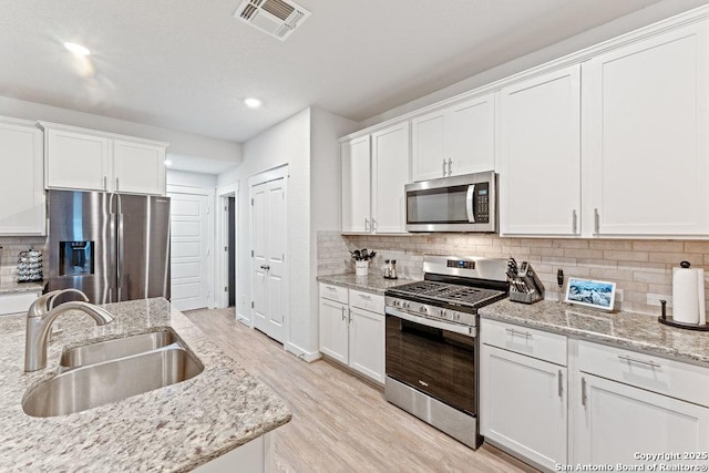 kitchen with visible vents, light wood-style floors, white cabinets, a sink, and stainless steel appliances