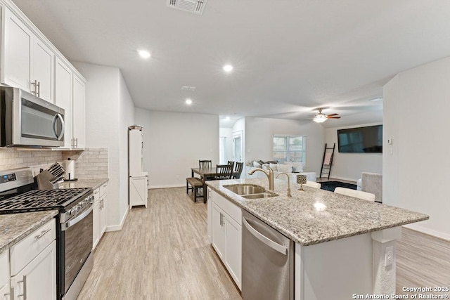 kitchen featuring visible vents, a kitchen island with sink, a sink, light wood finished floors, and appliances with stainless steel finishes
