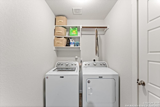 clothes washing area with laundry area, a textured ceiling, visible vents, washing machine and dryer, and a textured wall
