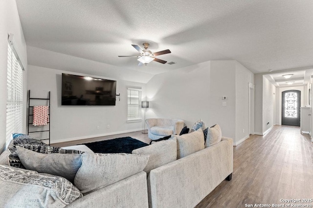 living area with ceiling fan, a textured ceiling, baseboards, wood finished floors, and visible vents