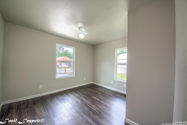 spare room with a ceiling fan, baseboards, a wealth of natural light, and dark wood-type flooring