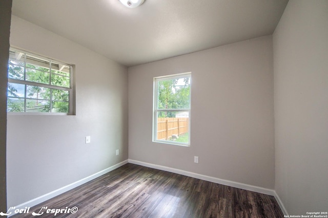 empty room featuring baseboards, dark wood-style flooring, and a wealth of natural light