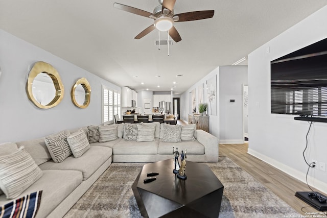 living room featuring light wood-type flooring, baseboards, ceiling fan, and visible vents
