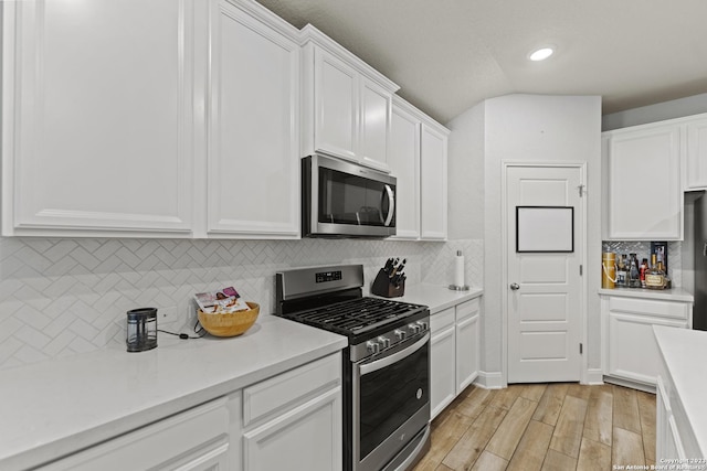 kitchen with white cabinets, appliances with stainless steel finishes, light countertops, light wood-style flooring, and decorative backsplash