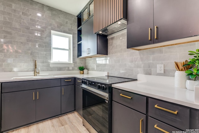 kitchen with a sink, light countertops, light wood-style flooring, tasteful backsplash, and range with electric stovetop