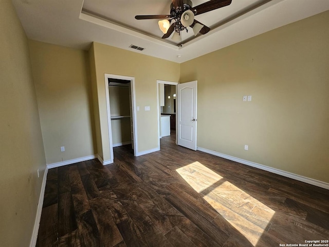 unfurnished bedroom with visible vents, dark wood finished floors, baseboards, a closet, and a tray ceiling