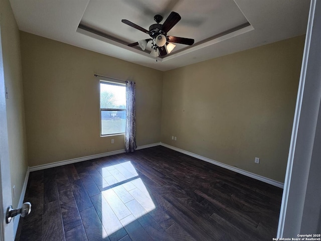 spare room with baseboards, a raised ceiling, ceiling fan, and dark wood-style floors