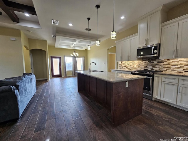 kitchen featuring backsplash, appliances with stainless steel finishes, arched walkways, a center island with sink, and a sink