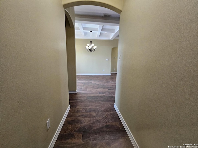 hall featuring visible vents, arched walkways, beamed ceiling, a notable chandelier, and coffered ceiling