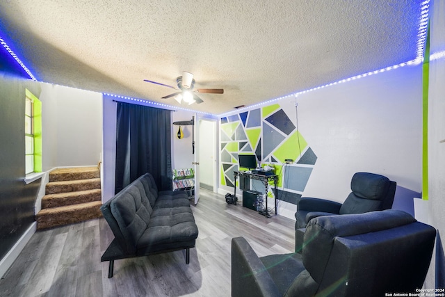living room with ceiling fan, a textured ceiling, wood finished floors, stairway, and baseboards
