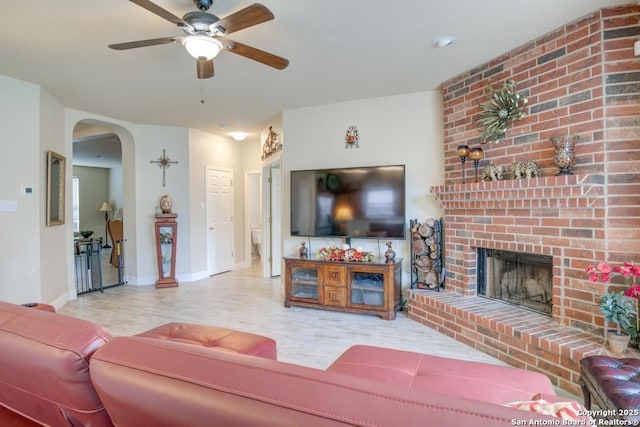living area with ceiling fan, a brick fireplace, arched walkways, baseboards, and wood finished floors