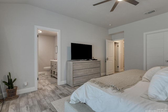 bedroom featuring visible vents, baseboards, light wood-type flooring, ensuite bath, and vaulted ceiling