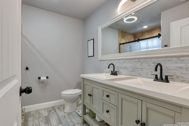 full bath with double vanity, backsplash, a shower stall, a sink, and baseboards