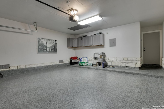 garage featuring visible vents, a garage door opener, and electric panel