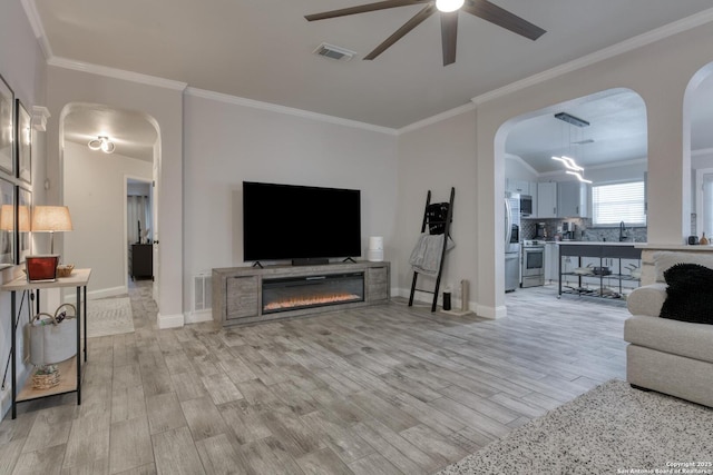 living area featuring visible vents, arched walkways, ceiling fan, and light wood-type flooring