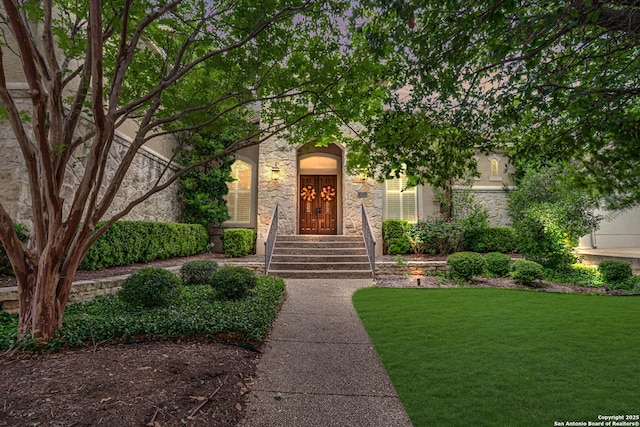 entrance to property featuring a lawn and stone siding