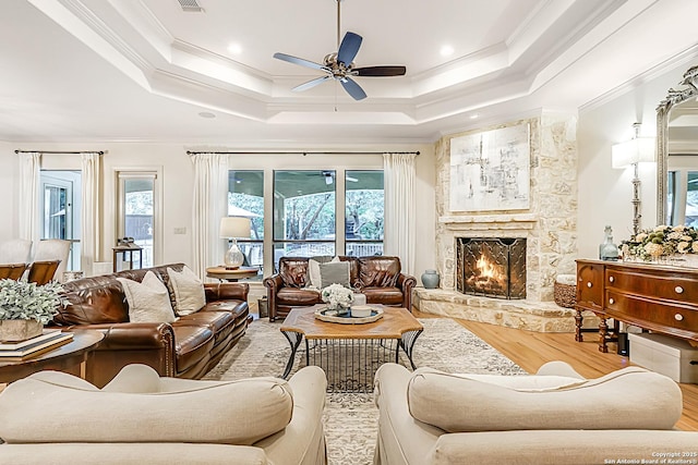 living area with ceiling fan, plenty of natural light, wood finished floors, and a tray ceiling