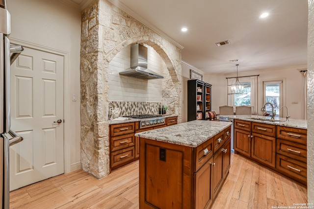 kitchen with brown cabinetry, wall chimney exhaust hood, crown molding, and stainless steel gas stovetop