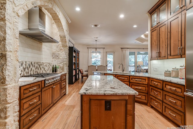kitchen featuring visible vents, decorative backsplash, wall chimney range hood, a sink, and stainless steel gas stovetop