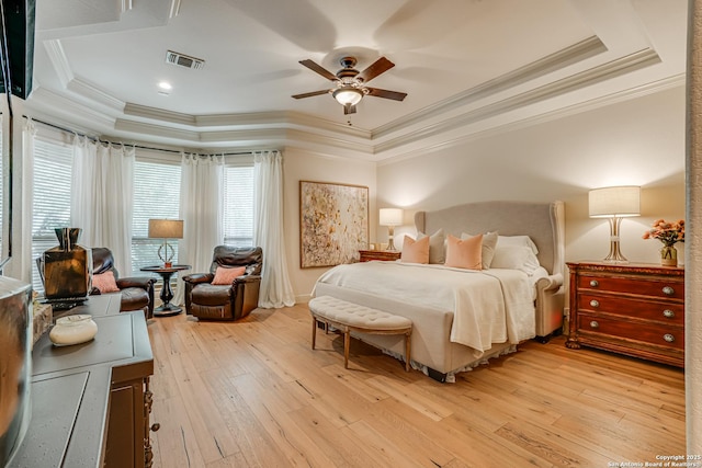 bedroom with visible vents, ornamental molding, a tray ceiling, a ceiling fan, and light wood-style flooring
