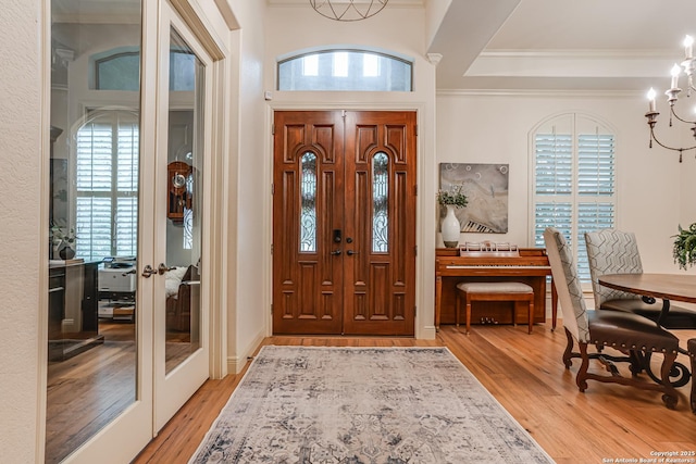 entryway with an inviting chandelier, crown molding, french doors, and light wood-style flooring