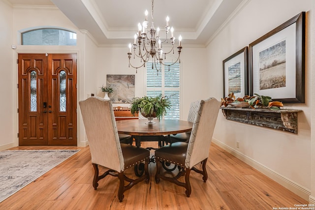 dining area featuring an inviting chandelier, ornamental molding, baseboards, a raised ceiling, and light wood-style flooring
