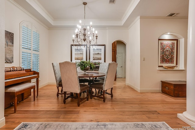 dining room with a notable chandelier, a raised ceiling, light wood-style floors, arched walkways, and visible vents