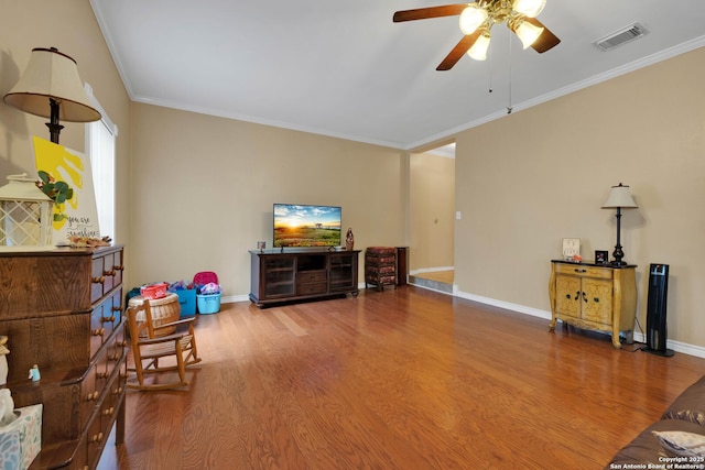 living area with visible vents, ornamental molding, wood finished floors, baseboards, and a ceiling fan
