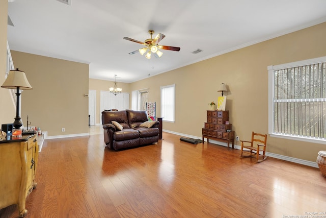 living area with crown molding, light wood-style flooring, ceiling fan with notable chandelier, baseboards, and visible vents
