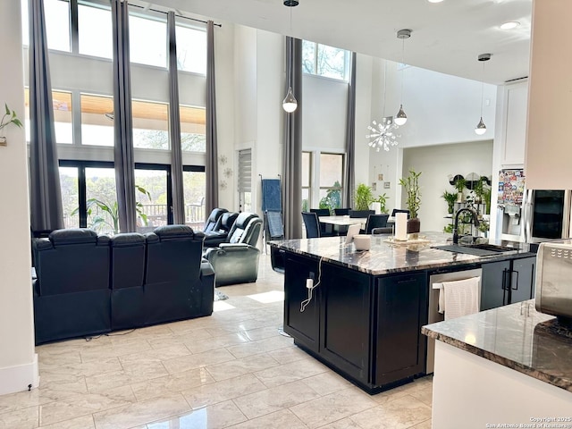 kitchen featuring pendant lighting, a sink, dark cabinets, dark stone counters, and a high ceiling
