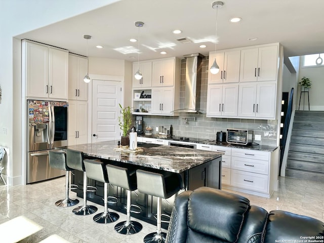 kitchen with stainless steel fridge, a breakfast bar area, wall chimney exhaust hood, white cabinetry, and backsplash