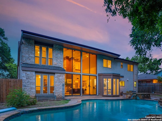 rear view of house with a fenced in pool, fence, and stone siding