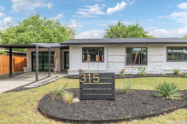 view of front of property featuring fence, stone siding, board and batten siding, concrete driveway, and a carport