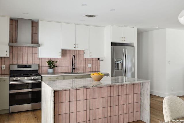 kitchen with wall chimney range hood, a sink, light wood-style flooring, stainless steel appliances, and tasteful backsplash