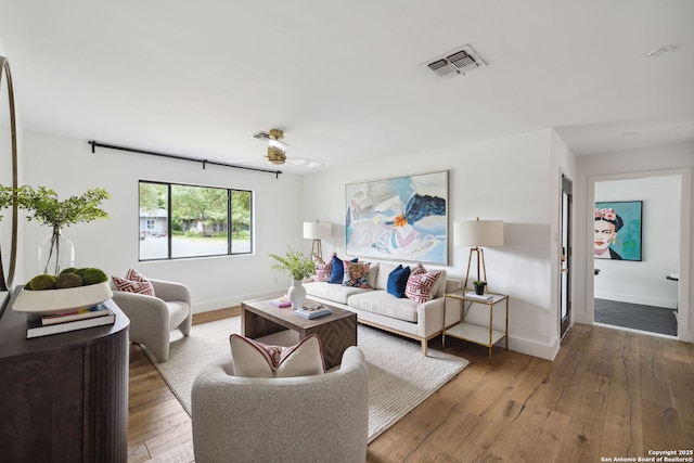 living area with baseboards, a ceiling fan, hardwood / wood-style floors, and visible vents