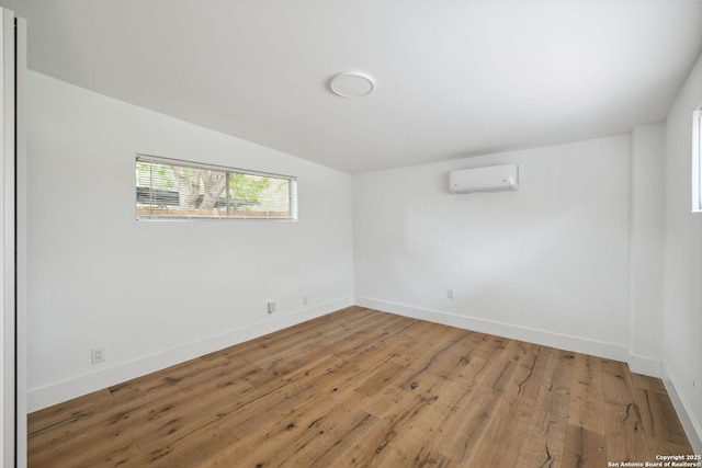 spare room with baseboards, vaulted ceiling, a wall unit AC, and light wood-type flooring