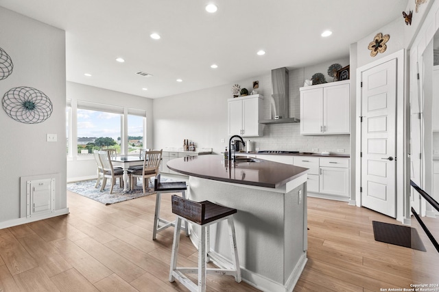 kitchen featuring wall chimney range hood, visible vents, dark countertops, light wood-type flooring, and a sink