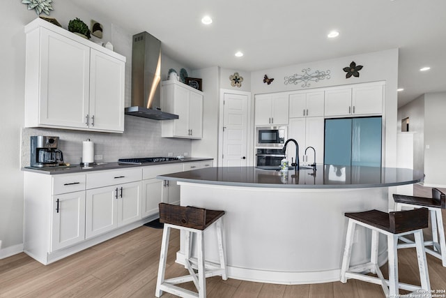 kitchen featuring wall chimney range hood, built in appliances, light wood-type flooring, and dark countertops